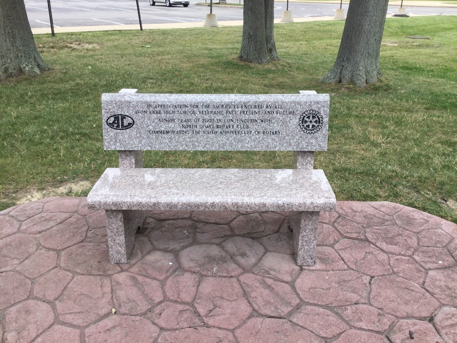 A granite memorial bench standing on a paved area
