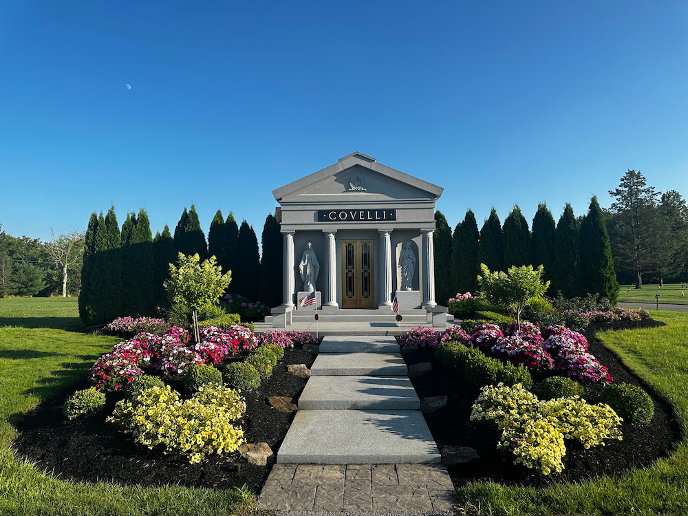 The Covelli family mausoleum in grey granite, columns and bronze doors, surrounded by planting