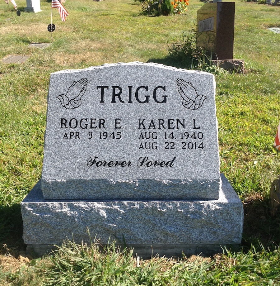 A slant granite memorial set on a base in a cemetery lawn