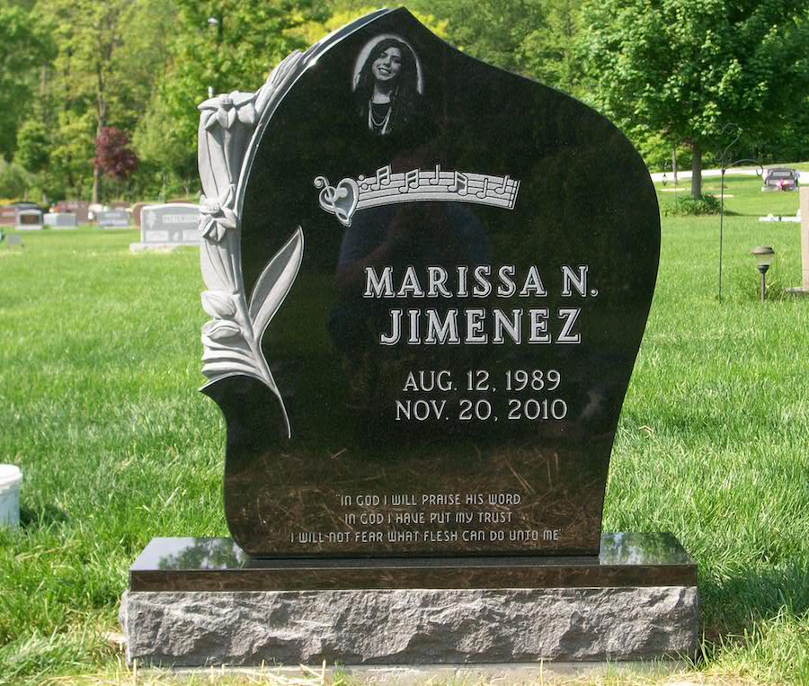A polished dark granite upright monument standing in a cemetery lawn